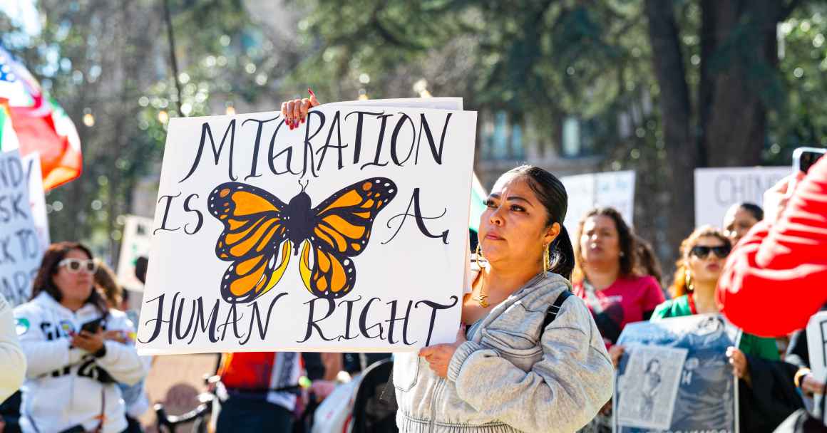 A woman is attending an immigrant rights protest and holds a signs with an image of a butterfly that says "migration is a human right"