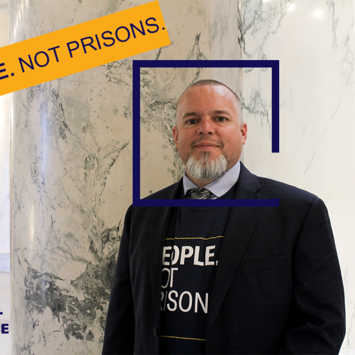 Jason is a tanned middle aged man with a salt and pepper beard, looking pleasantly at the camera from inside the marble rotunda in the Idaho State Capitol Building.