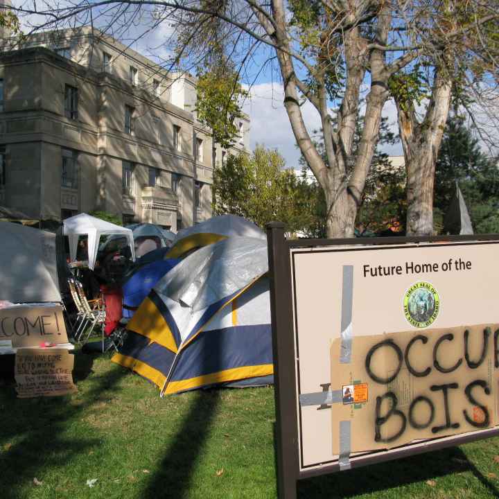 Occupy Boise a sign with a cardboard sign taped on top with spray painted "occupy boise" on it with tents in the background