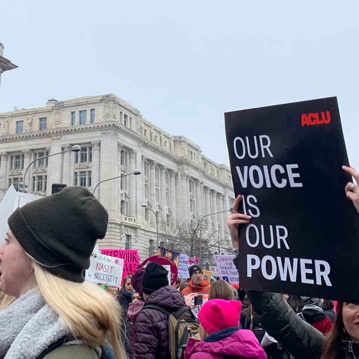 A protestor holding a sign with an ACLU logo that says Our Voice is Our Power.
