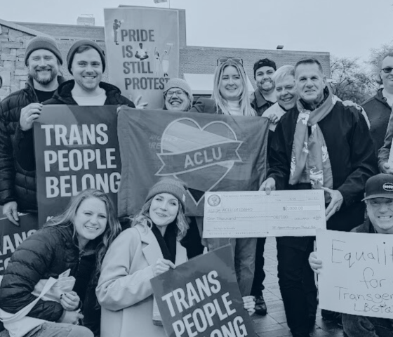 Blue tinted picture of ACLU staff holding signs that say Trans People Belong and Pride is Still Protest